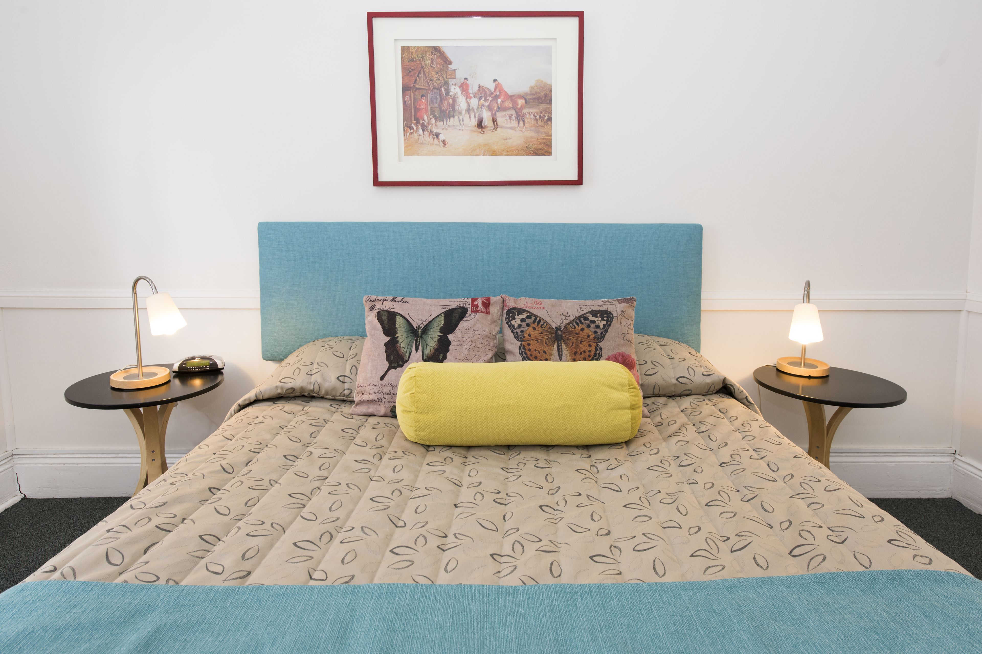 A neatly made bed with a patterned bedspread, two bedside tables with lamps, and a framed picture on the wall.