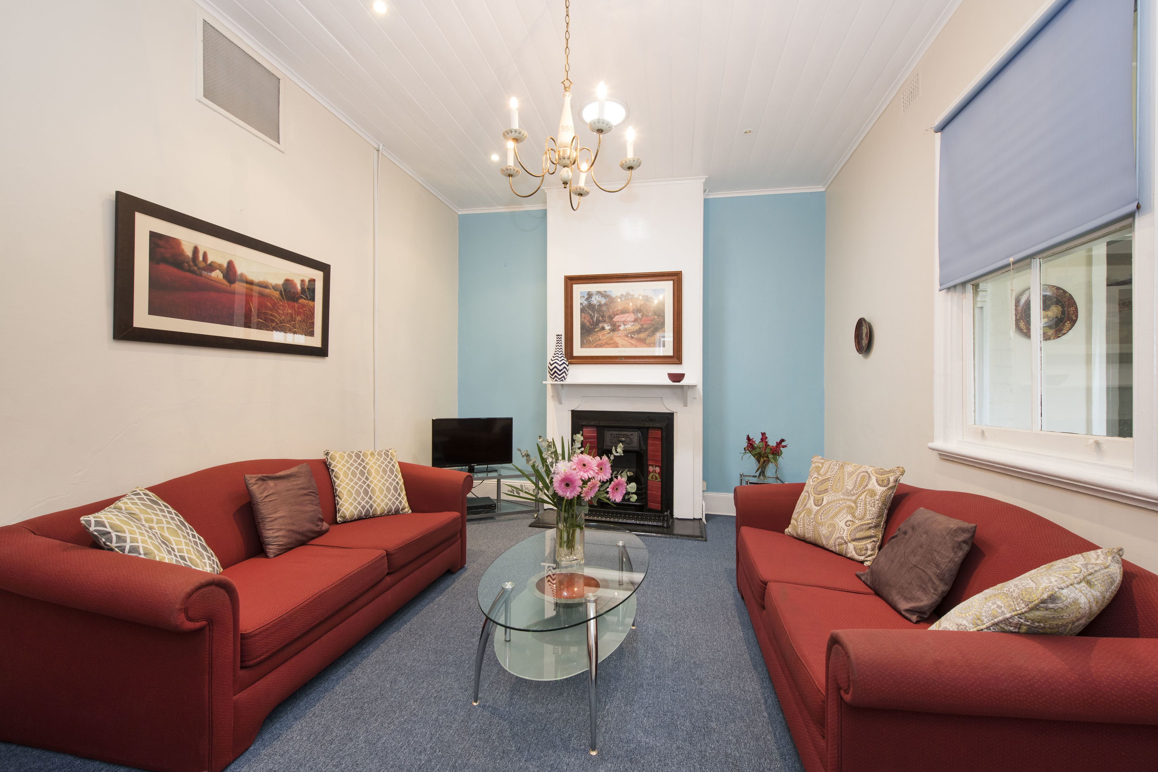 A living room with two red sofas, a glass coffee table, a fireplace, and a mounted television.