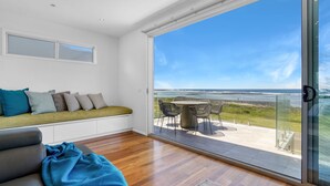 A balcony with a view of the ocean, a seating area with cushions, and a table with chairs. - Offering breathtaking views of South Beach (Port Fairy)