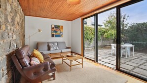 A living room with a leather sofa, a wooden coffee table, and a large sliding glass door leading to an outdoor patio. - A bluestone cottage in the heart of Port Fairy (Port Fairy)