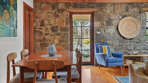 A dining area with a wooden table and chairs, a blue vase, and a stone wall. - A bluestone cottage in the heart of Port Fairy (Port Fairy)