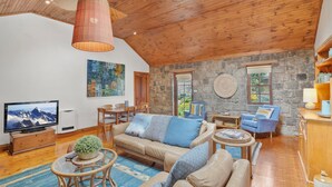 A spacious living room with a stone wall, wooden ceiling, and a large TV. - A bluestone cottage in the heart of Port Fairy (Port Fairy)