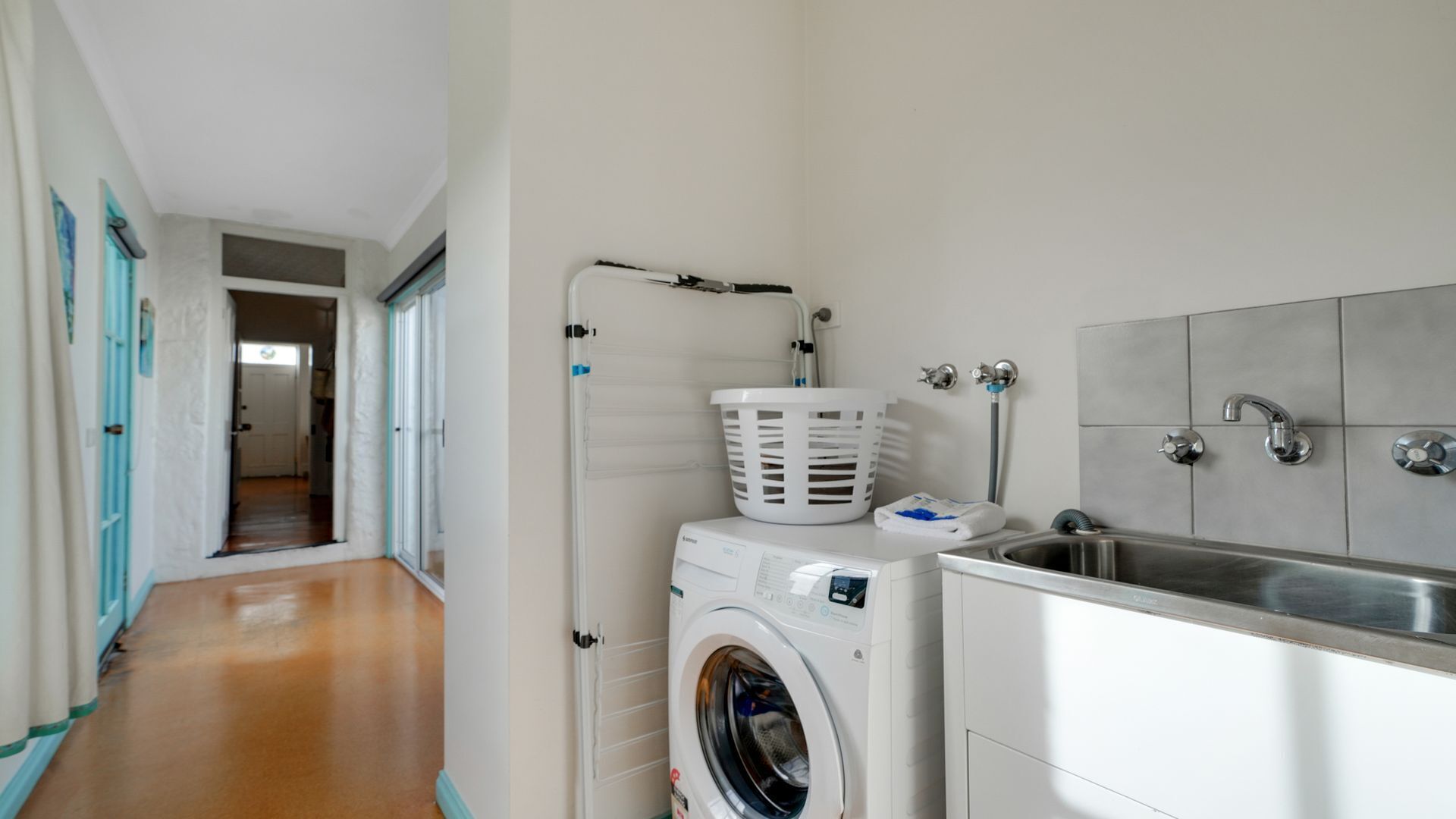 A laundry room with a washing machine, a drying rack, and a sink.