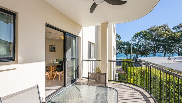 Un balcon avec une table en verre, des chaises et une vue sur la mer.
