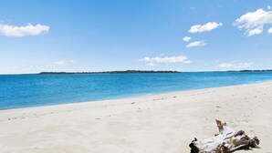 Une plage à l’eau d’un bleu limpide, bordée d’un rivage sablonneux, avec une terre lointaine à l’horizon.