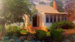 A single-story house with a front porch, a chimney, and a garden with various plants and shrubs. - AMITY WINE COTTAGE – Wonderful Vintage Charm and Décor in Oregon Wine Country (Amity)