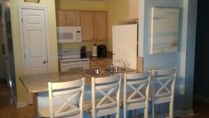 A compact kitchen with a microwave, stove, and coffee maker. There is a dining area with a table and chairs.