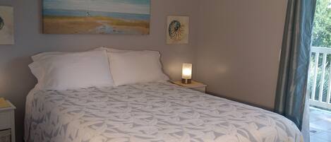 Un dormitorio con cama, ventilador de techo, un cuadro y una mesita de noche.