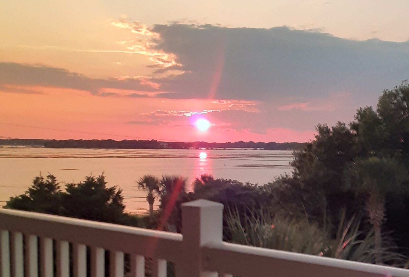 A sunset over a body of water with a distant shoreline and vegetation in the foreground.