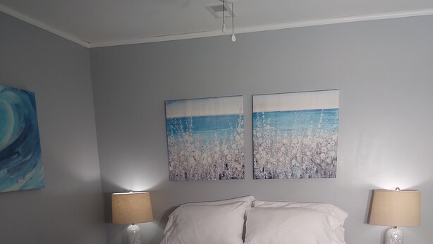 A bedroom with a bed, two nightstands, a ceiling fan, and two wall-mounted paintings.