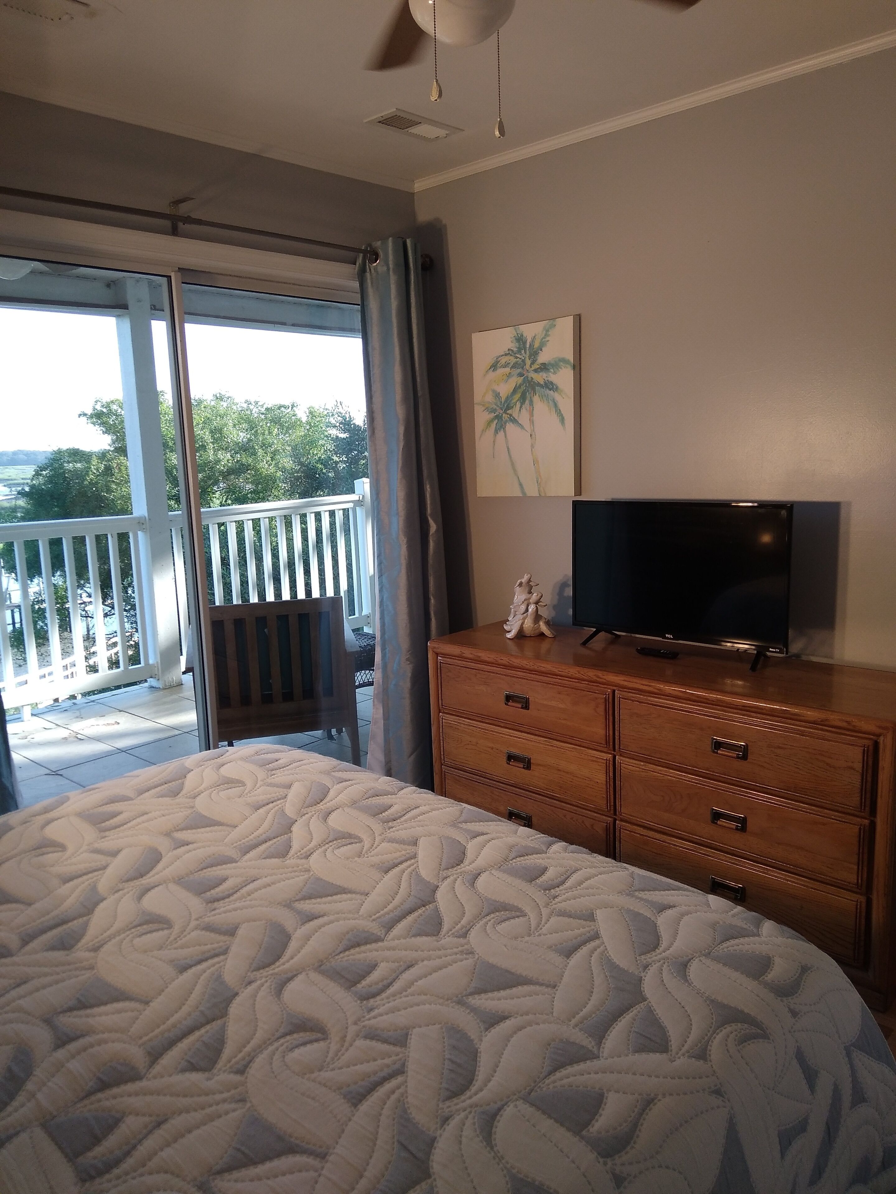 Un dormitorio con una cama grande, un aparador de madera, una televisión y vistas a un balcón con barandilla.
