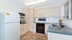 Compact kitchen with modern design, light cabinetry, and stainless steel sink, featuring a refrigerator, microwave, toaster, and oven.