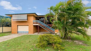 Two-story building with a garage and staircase, set amidst a manicured lawn and lush greenery.