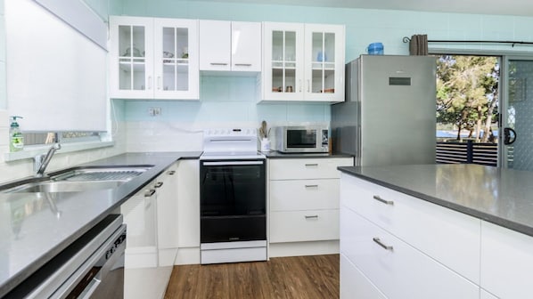 A modern kitchen with white cabinets, a stainless steel sink, a built-in oven, and a microwave.
