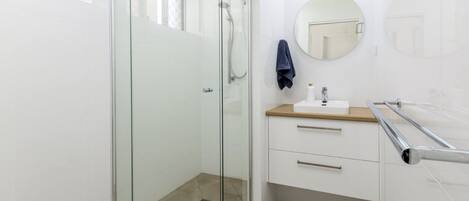 Een moderne badkamer met een douchecabine van glas, een witte wastafel met een houten blad, een ronde spiegel en een handdoek aan de muur.