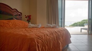Una cama grande con colcha naranja, cabecero de madera y un jarrón con flores rojas.