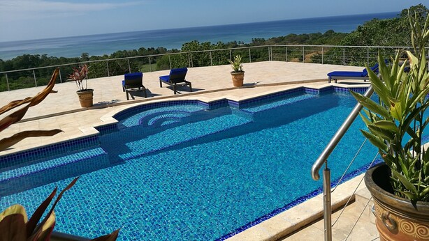 Piscina con vista despejada al océano, rodeada de sillas de descanso y plantas en macetas.
