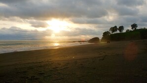 Una playa con el sol poniéndose en el horizonte, un promontorio rocoso y algunas personas caminando.