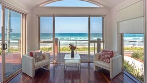 Una habitación con un gran ventanal que da a una vista de la playa, dos sofás, una mesita y un florero con flores.