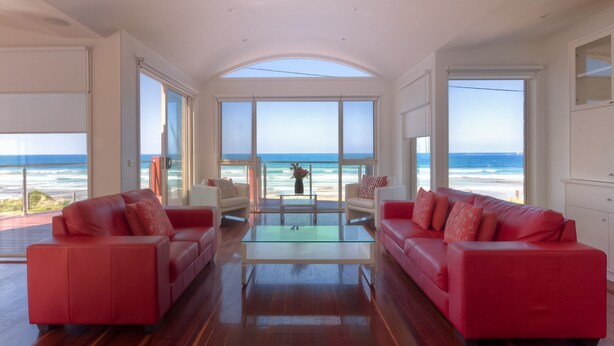 Amplio salón con grandes ventanales con vista al océano, con sofás rojos y una mesa de centro de vidrio.