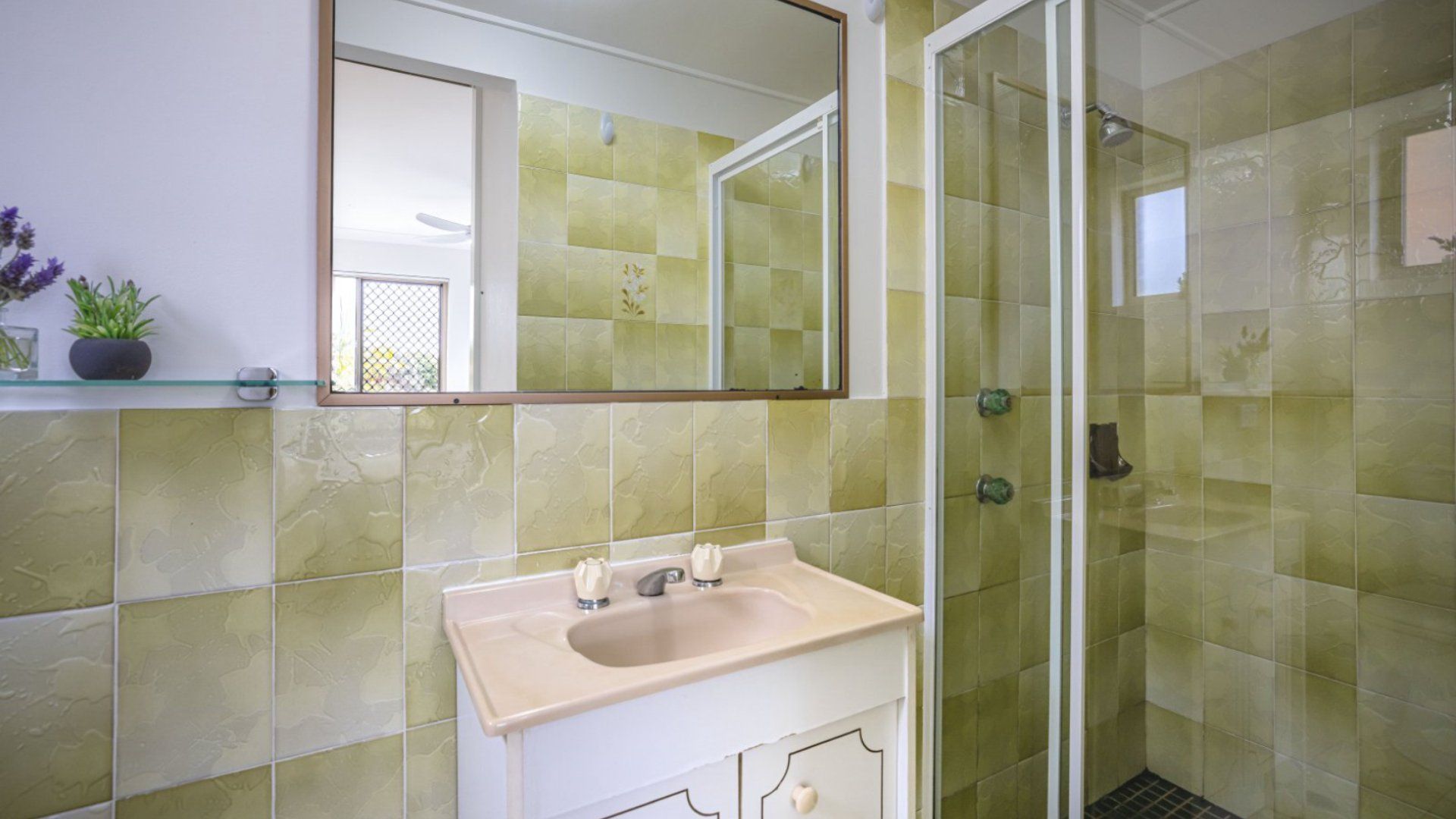 A bathroom with a glass shower enclosure, a sink with two faucets, and a mirror above the sink.