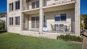 A multi-story building with a balcony on the ground floor, a sign indicating holiday rental availability, and a well-maintained lawn. - Bribie Horizons on Boyd (WOORIM)