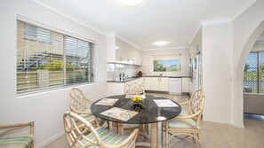A modern kitchen with white cabinets, a round glass table, and wicker chairs. - Bribie Horizons on Boyd (WOORIM)
