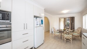 Una cucina moderna con mobili bianchi, un forno a microonde, un forno e un frigorifero. C'è un'area pranzo con tavolo e sedie.