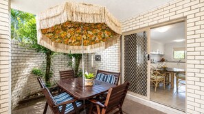 A patio with a wooden table and chairs, a decorative umbrella, and a brick wall. - Bribie Horizons on Boyd (WOORIM)