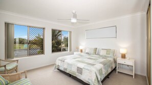 A bedroom with a bed, two bedside tables, a chair, and a ceiling fan. - Bribie Horizons on Boyd (WOORIM)