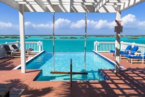 Zona de piscina con sillón colgante, sillas de descanso y señal de prohibición de saltos.