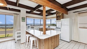 Une cuisine dotée d’un grand îlot central, de poutres en bois, d’une vue sur la plage et d’un réfrigérateur.