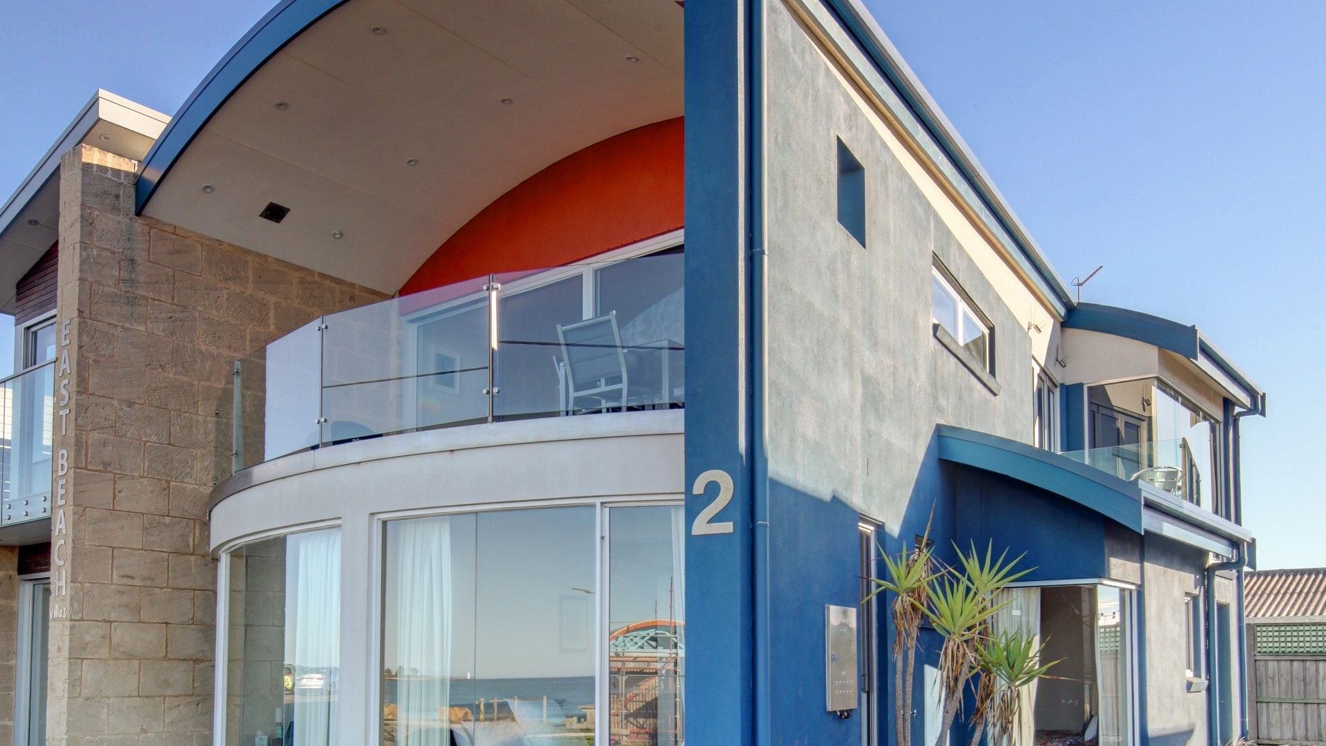 A modern two-story building with a curved balcony, large windows, and a visible number '2' on the facade.