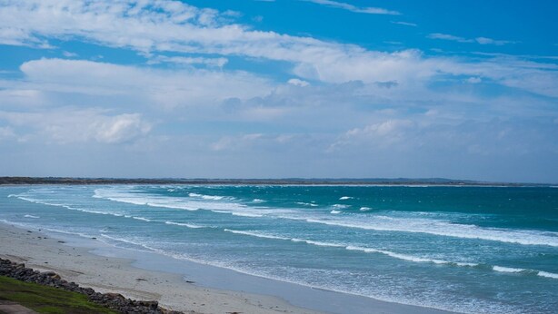 Ein Strand mit Wellen, einem klaren Himmel und weiter Land.