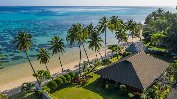 Vista de playa con palmeras, un edificio de techo de paja y agua azul cristalina.