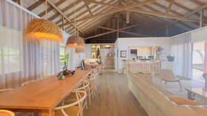 Un comedor amplio con una larga mesa de madera y sillas, una cocina con barra y ventanas grandes que dejan entrar luz natural.