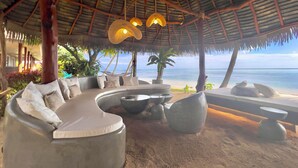 Un salón junto a la playa con una zona de estar curvada, una chimenea y vistas al océano.