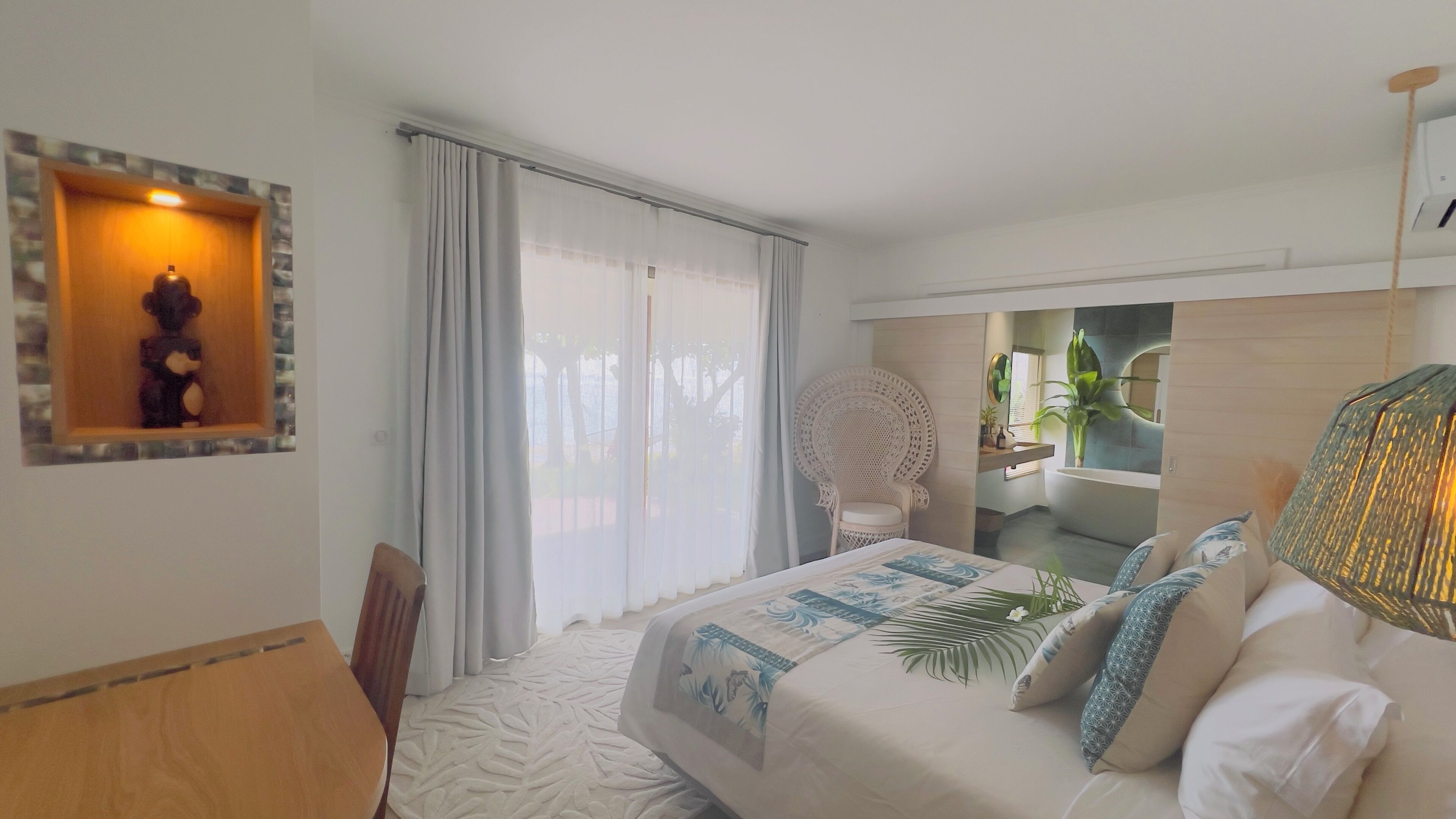 Une chambre d’hôtel avec un lit, une chaise, un bureau, une fenêtre avec des rideaux et une salle de bain visible à travers une porte ouverte.