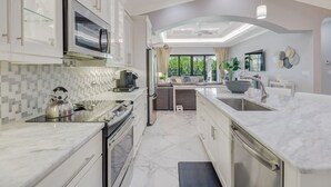 Una cucina moderna con forno integrato, microonde e macchina del caffè. C'è un'area pranzo con un divano e un'ampia finestra.