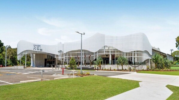 A modern building with a curved facade, a prominent entrance, and a landscaped area in front.