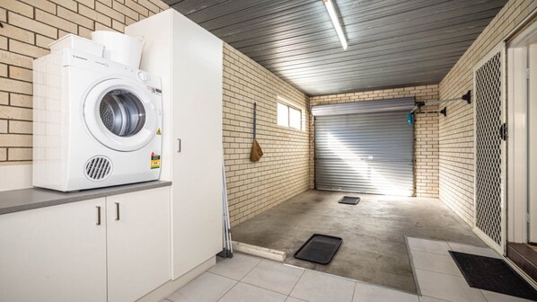 A laundry room with a washing machine, a broom, and a closed garage door. - Great Views, Ground Floor Unit (BONGAREE)