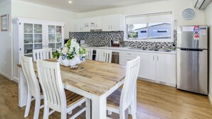 Una cocina moderna con armarios blancos, una mesa de comedor de madera y un refrigerador de acero inoxidable.