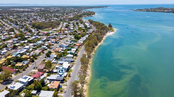 An aerial view of a coastal residential area with houses, a road, and a beach.