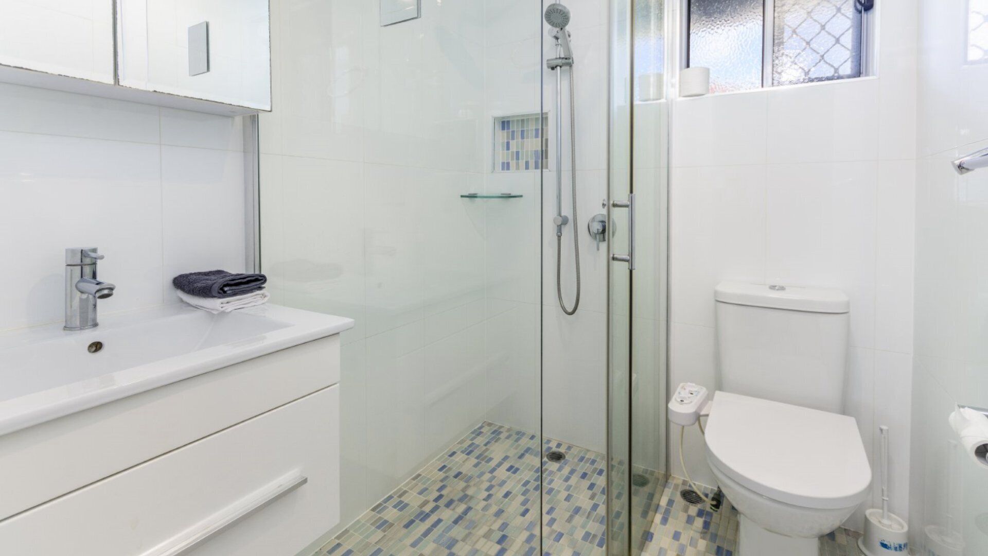 A bathroom with a glass-enclosed shower, a white toilet, and a sink with a towel.