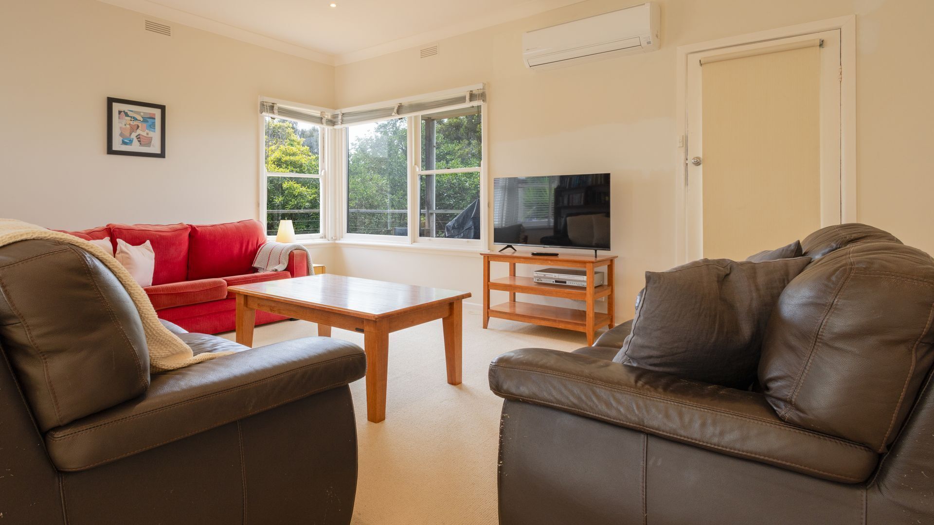 A living room with two leather sofas, a red sofa, a wooden coffee table, and a television on a wooden stand.