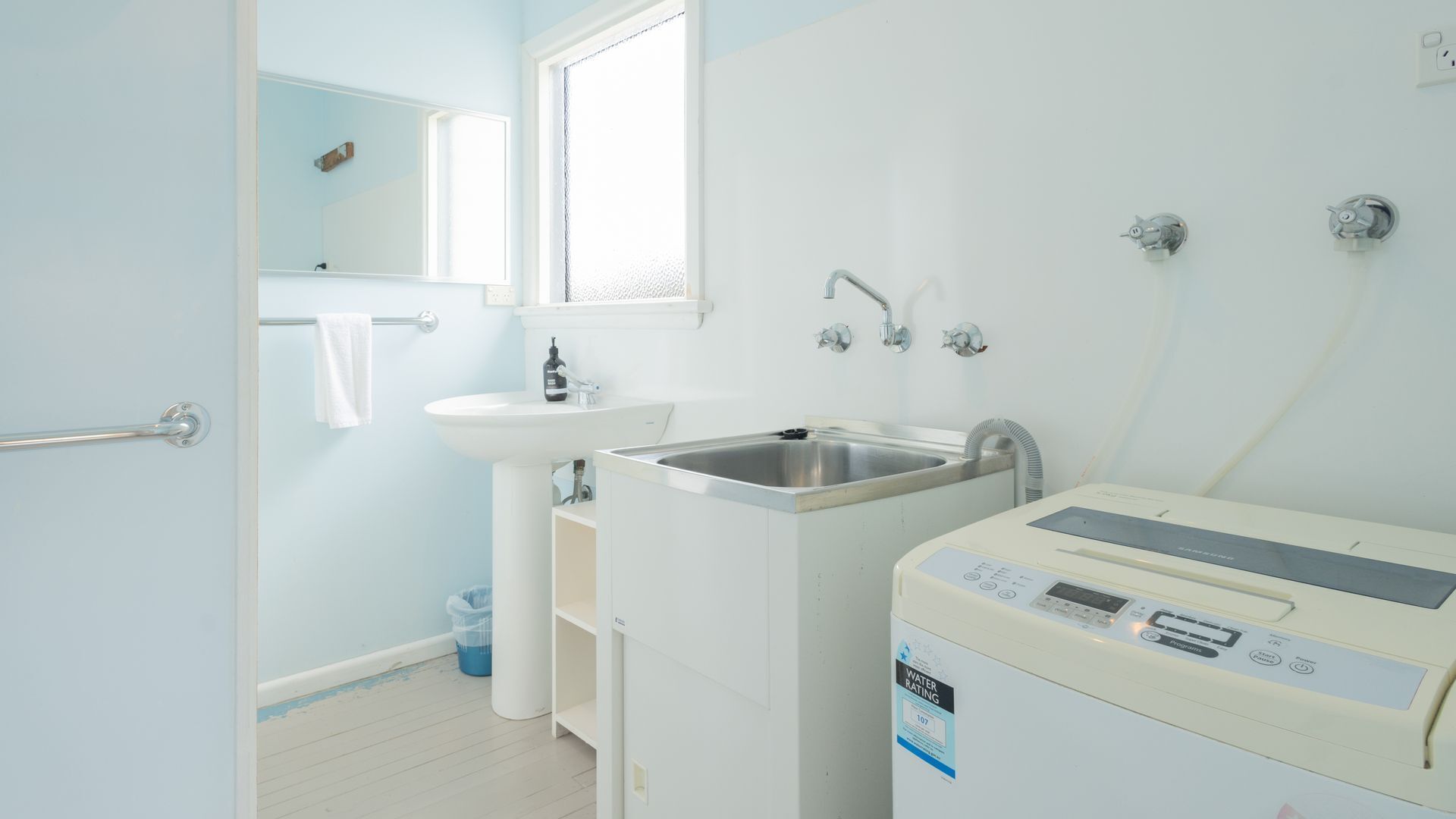 Un baño con lavamanos blanco, un espejo, una ventana, toallero y calentador de agua.