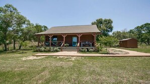 Une cabane en bois avec un porche, une porte bleue et un petit abri de jardin, le tout situé dans une zone herbeuse.