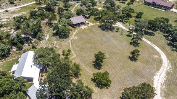 An aerial view of a property with a large open grassy field, a few scattered trees, and a few buildings with distinct roofs.