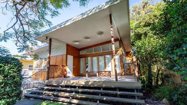 Une maison moderne dotée d’un porche abrité, d’un escalier en bois et de grandes fenêtres.