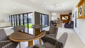 A spacious living area with a round wooden table surrounded by patterned chairs, a kitchen in the background, and a view through large sliding glass doors.